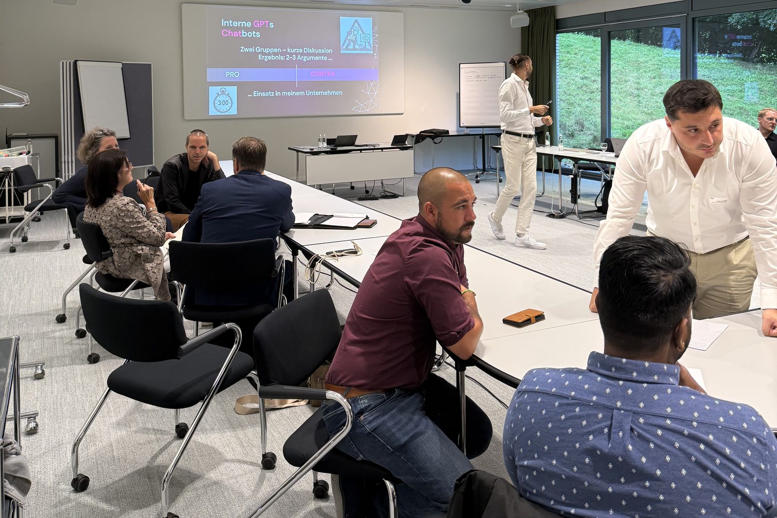 Workshop-Teilnehmende diskutieren in Gruppen, vorne die Aufgabe «Interne GPTs & Chatbots: PRO und CONTRA»