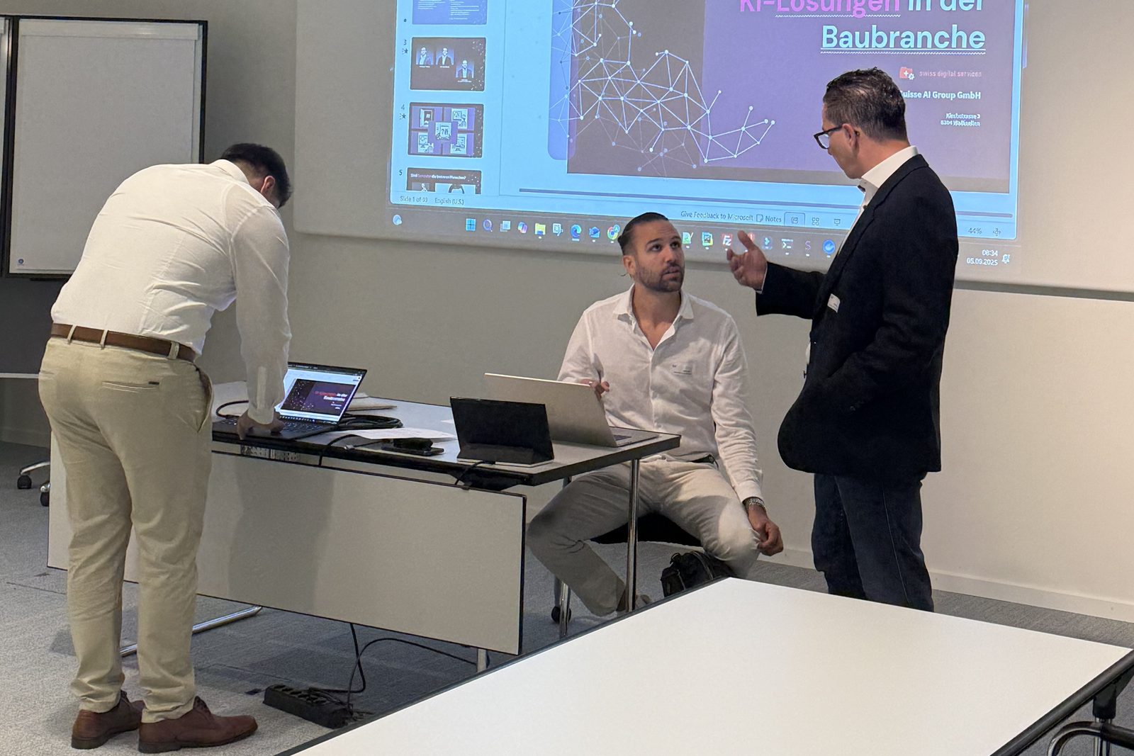Vorbereitung vor dem Workshop: Laptops werden angeschlossen, auf der Leinwand die Titelfolie «KI-Lösungen in der Baubranche»