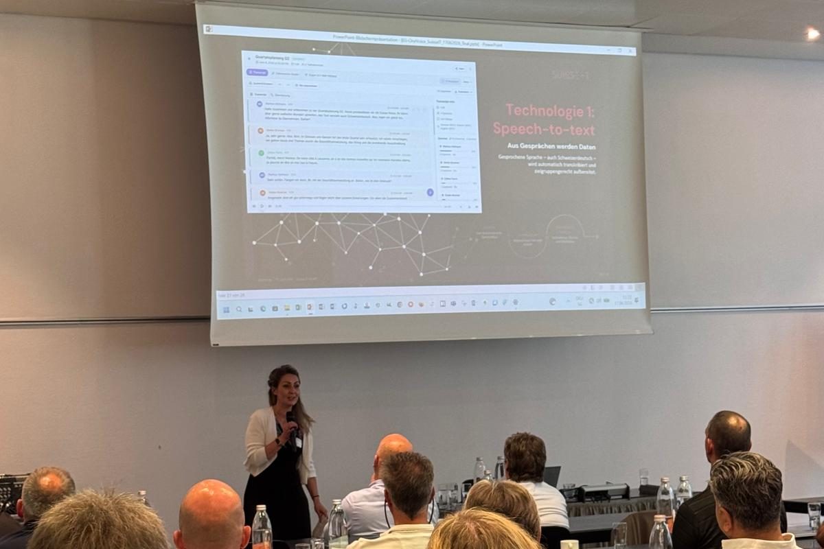 Referentin mit Mikrofon präsentiert eine Live-Transkription unter dem Titel «Speech-to-text: Aus Gesprächen werden Daten»